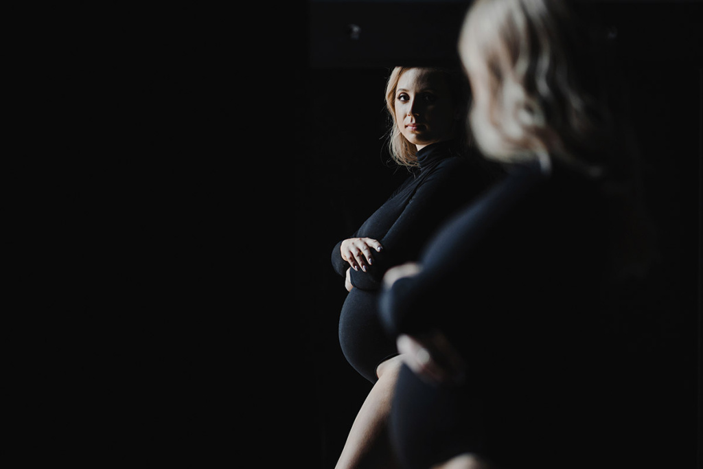 pregnant-blonde-woman-black-bodysuit-stands-near-mirror-looks-her-reflection.jpg